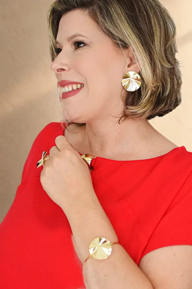 Branca Pedroso de perfil, sorrindo, com vestido vermelho, brinco, anel e pulseira dourados