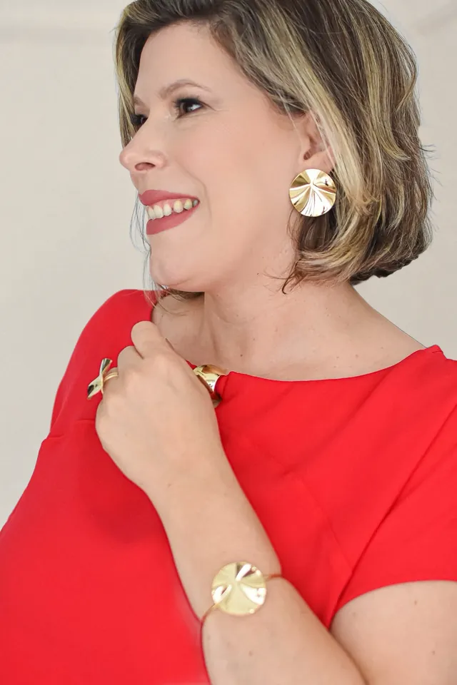 Branca Pedroso de perfil, sorrindo, com vestido vermelho, brinco, anel e pulseira dourados